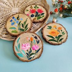 four wooden coasters with flowers painted on them sitting in front of a wicker basket