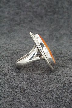 This spiny oyster and sterling silver ring was made by Navajo silversmith Chris Nez. The inside of the band is signed CN and stamped sterling.Size: 6.5Length: 1 1/4"Width: 1"Free shipping on all orders! We ship with USPS and always include tracking. All orders ship within a day of payment.Returns are accepted up to 30 days after you receive your order. Just send us a message. Our shop offers cash back or store credit. The item must be returned in new condition. Sterling Silver Orange Ring With Polished Finish, Orange Sterling Silver Ring With Polished Finish, Orange Oval Sterling Silver Ring, Formal Sterling Silver Rings With Inlay, Collectible Orange Sterling Silver Jewelry, Southwestern Style Rings With Polished Finish, Spiny Oyster, Sterling Silver Ring, The Band