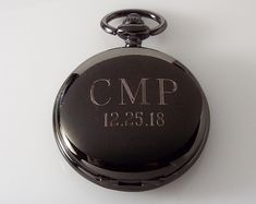 "This gorgeous watch features a black dial with bright copper color numbers and ornate white hands. The skeleton center gives you a glimpse of some of the wheels and cogs that make this pocket watch run! This pocket watch measures 1 7/8\" in diameter and includes a 14\" removable watch chain. Both front and back of this pocket watch can be engraved, so you can personalize the front with a name, initials, or a monogram, then a date or short message on the back (for a total of 50 letters). Or you Timeless Black Watch Accessories For Anniversary, Black Watches With Metal Dial For Anniversary, Black Skeleton Dial Watch As Gift, Black Pocket Watch With Metal Dial As Gift, Vintage Black Watch With Skeleton Dial, Black Engraved Watch Accessories As Gift, Black Watches For Anniversary With Round Dial, Black Stainless Steel Watch Accessories For Gift, Black Stainless Steel Watch Accessories As Gift