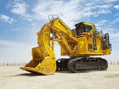 a large yellow machine sitting on top of a dirt field next to a blue sky