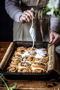 a person is spreading icing on rolls in a pan