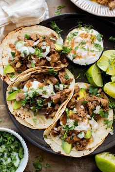 three tacos on a plate with limes and cilantro