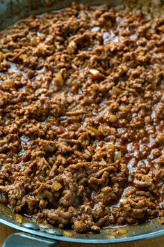 a pan filled with meat and sauce on top of a wooden table