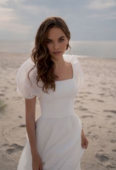 a woman standing on top of a sandy beach next to the ocean wearing a white dress