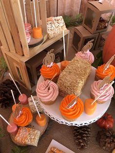 an assortment of cupcakes and desserts displayed on a cake stand with pine cones