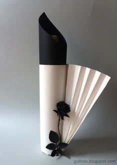 a black and white vase with a rose on it's side, sitting against a gray background