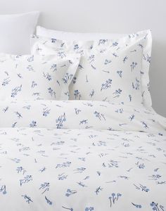 a bed with white sheets and blue flowers on the comforter, along with two pillows