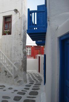 an alley way with white buildings and blue balconies on either side, leading up to the second story