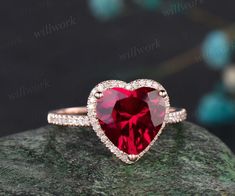 a red heart shaped ring on top of a rock with diamonds around the band and inside