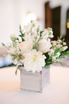 white flowers are in a square vase on a table