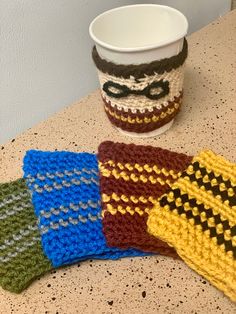 four crocheted coasters sitting on top of a counter next to a cup