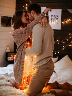 a man and woman are kissing in bed with lights on the wall behind them at night