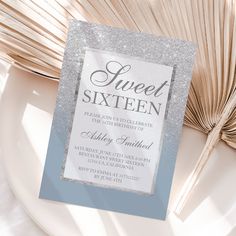 a silver glitter sweet sixteen party card on a white plate with fan in the background