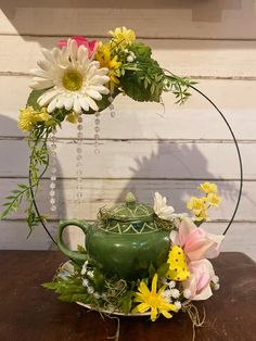 a green teapot with flowers and greenery in it sitting on a wooden table