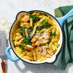 a skillet filled with pasta and chicken on top of a marble counter next to a spatula