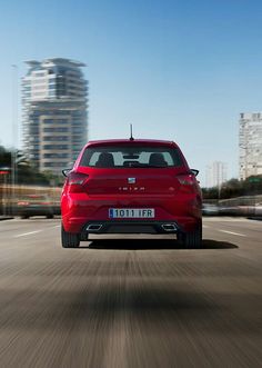 the rear end of a red car driving down a road in front of tall buildings