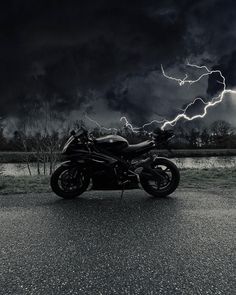 a motorcycle parked on the side of a road with lightning in the sky behind it