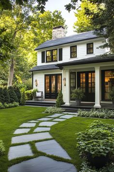 a white house with black shutters and stone walkway leading to the front door is surrounded by lush greenery