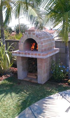 an outdoor brick pizza oven in the middle of a yard with palm trees around it