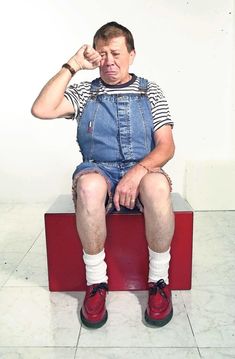 a man sitting on top of a red object with his fist up and hands behind his head