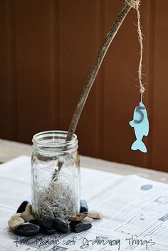 a glass jar filled with sand next to a wooden stick and some sea shells on top of a table