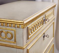 an ornate white and gold chest of drawers with two rings on the front door knobs