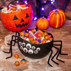 a bowl filled with candy sitting on top of a table next to two pumpkins