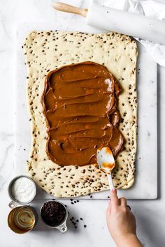 someone spreading peanut butter on top of an uncooked flatbread with chocolate spread