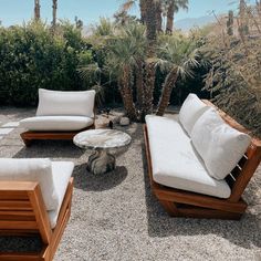 an outdoor seating area with palm trees in the background and white cushions on top of it