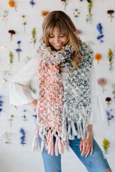 a woman standing in front of a wall with flowers on it wearing a multicolored scarf