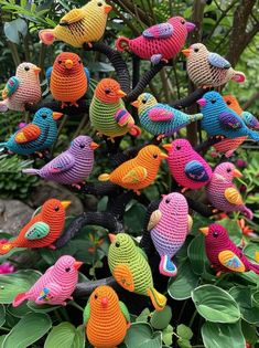 colorful crocheted birds sitting on top of a tree in a garden with green leaves