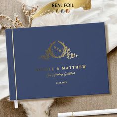 a blue book with gold foil on it next to a pen and some white feathers