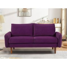 a purple couch sitting in a living room on top of a carpeted floor next to a lamp