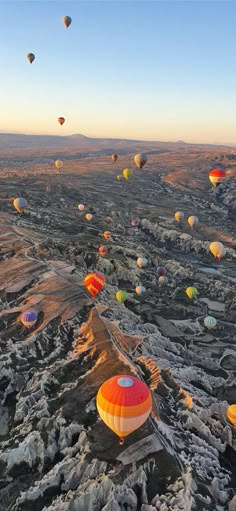 many hot air balloons are flying in the sky over rocks and mountains at sunrise or sunset