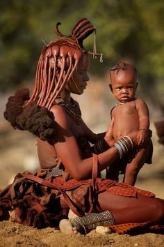 a woman holding a baby in her lap while sitting on top of a dirt ground