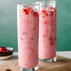 two glasses filled with ice and strawberries on top of a cutting board next to a bowl