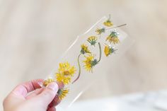 a hand holding a clear tube with yellow flowers in it