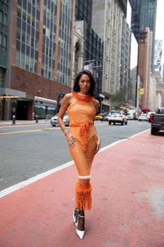 a woman in an orange dress is standing on the sidewalk