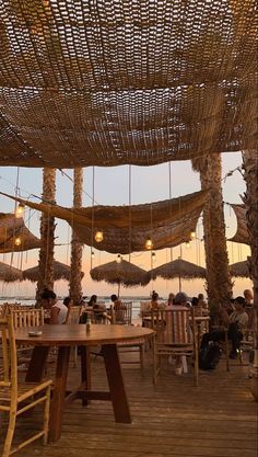 people are sitting at tables under umbrellas on the beach