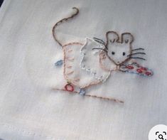 embroidered mouse on white linen with red and blue beadwork around the tail, hand stitched