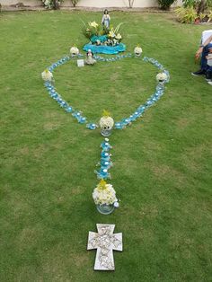 a blue and white floral arrangement in the shape of a cross on grass with people sitting around