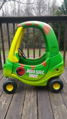 a green and yellow toy car sitting on top of a wooden deck next to a fence