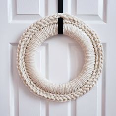 a white rope wreath hanging on the front door with a black handle and two rings attached to it