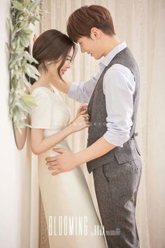 a young man and woman standing next to each other in front of a wall with flowers