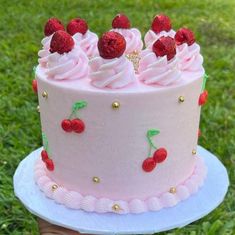 a pink cake with white frosting and raspberries on top, sitting in the grass