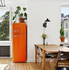 an orange refrigerator sitting in the middle of a room next to a table and chairs