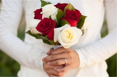 a woman holding a bouquet of red and white roses in her hands while wearing a wedding ring