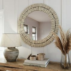 a round mirror sitting on top of a wooden table next to a vase and lamp