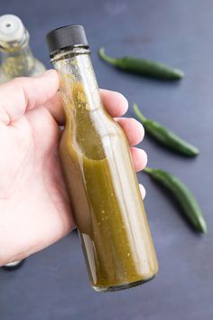 a hand holding a glass bottle filled with pickles next to some green chili peppers