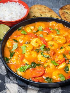 a black bowl filled with shrimp and rice next to some bread on a blue table cloth